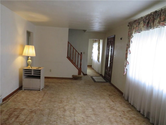 foyer featuring stairway, light colored carpet, and baseboards