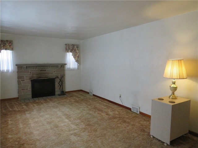 unfurnished living room with carpet flooring, visible vents, a stone fireplace, and baseboards