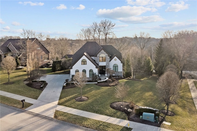 french provincial home with stone siding, driveway, and a front lawn