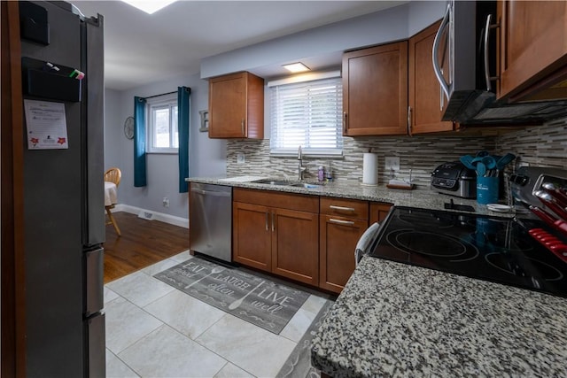 kitchen with tasteful backsplash, light stone counters, brown cabinetry, stainless steel appliances, and a sink