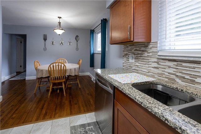 kitchen with light wood finished floors, light stone countertops, stainless steel dishwasher, brown cabinetry, and a sink