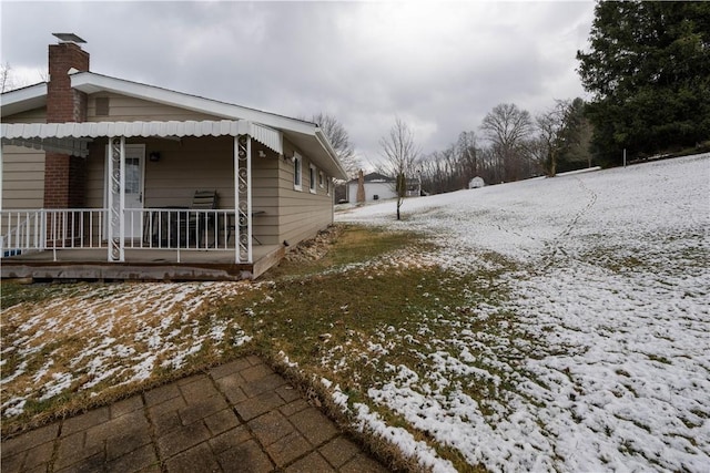 snow covered property with covered porch and a chimney