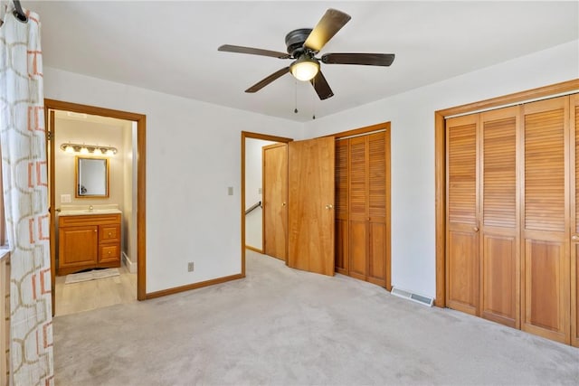 unfurnished bedroom with a ceiling fan, baseboards, multiple closets, light carpet, and connected bathroom