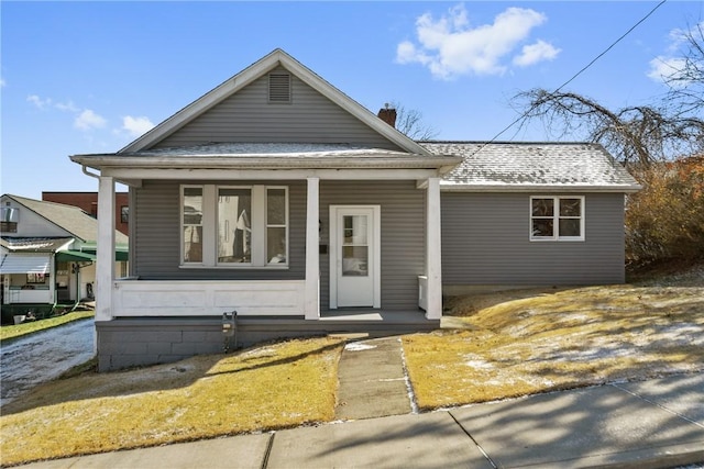 view of front of property with a chimney, covered porch, and a shingled roof