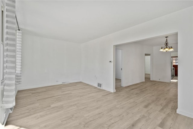 empty room with a chandelier, visible vents, light wood-type flooring, and baseboards