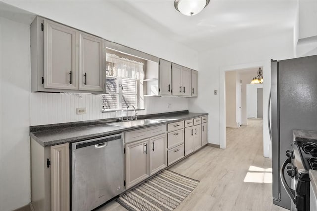 kitchen with dark countertops, gray cabinets, light wood-style floors, stainless steel appliances, and a sink