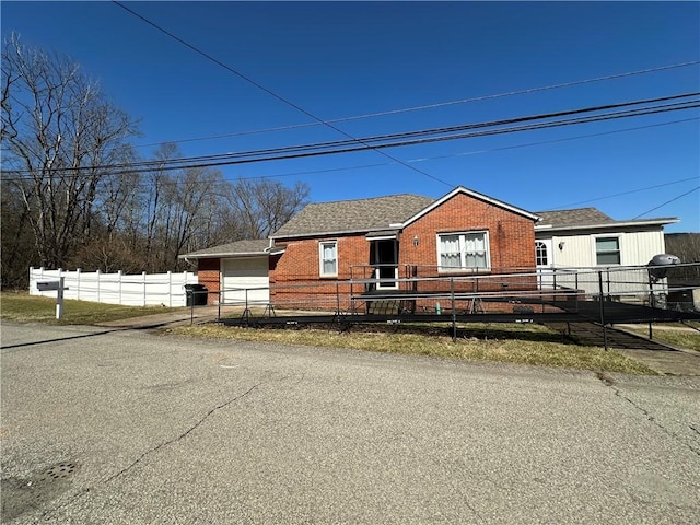 view of front facade with brick siding, a shingled roof, and fence