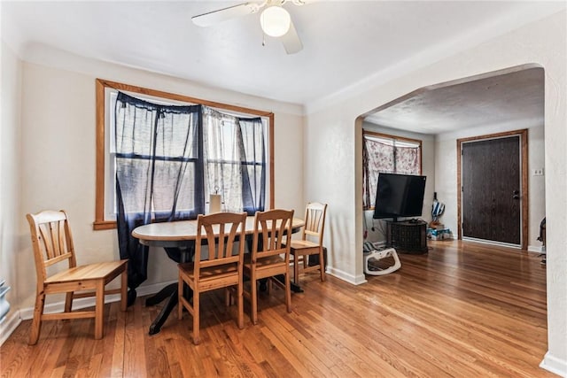 dining room featuring arched walkways, a ceiling fan, baseboards, and wood finished floors