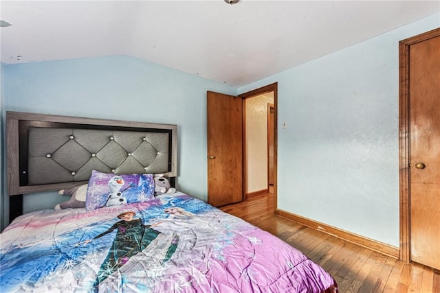 bedroom with baseboards, lofted ceiling, and hardwood / wood-style floors