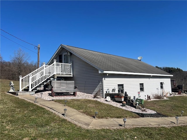 view of side of property with a yard, a shingled roof, and stairway