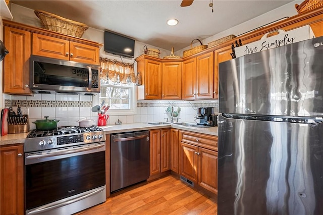 kitchen featuring brown cabinets, light countertops, light wood-style floors, appliances with stainless steel finishes, and tasteful backsplash