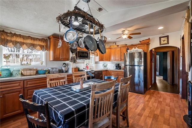 kitchen with arched walkways, light wood-style floors, appliances with stainless steel finishes, a textured ceiling, and brown cabinets