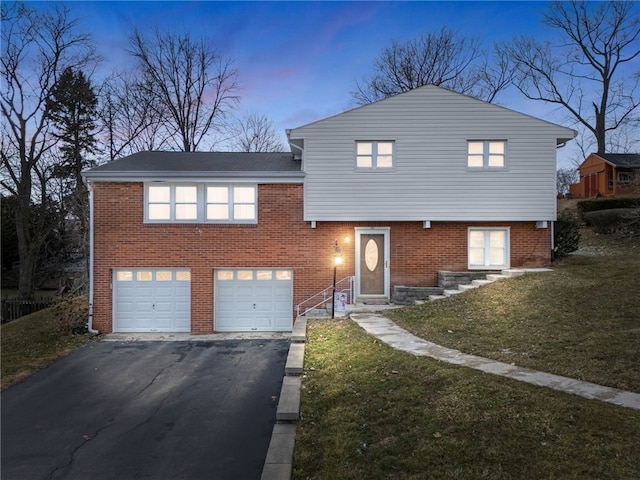 tri-level home featuring brick siding, driveway, an attached garage, and a yard