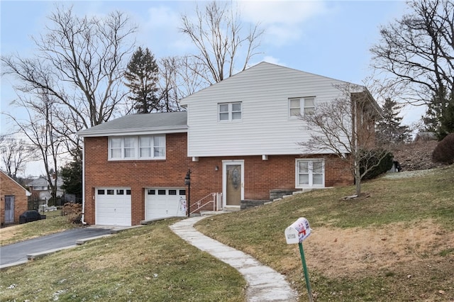 split level home with brick siding, a garage, driveway, and a front yard