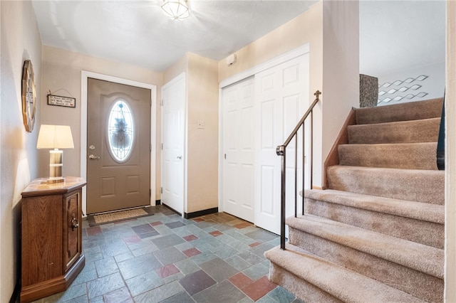 entrance foyer featuring baseboards, stone tile flooring, and stairs