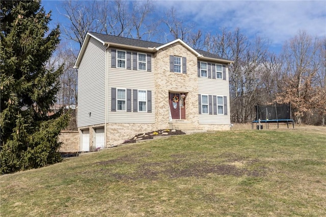 colonial-style house with brick siding, an attached garage, a front yard, and a trampoline