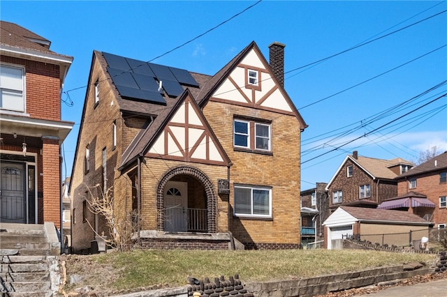 english style home with stucco siding, fence, brick siding, solar panels, and a chimney