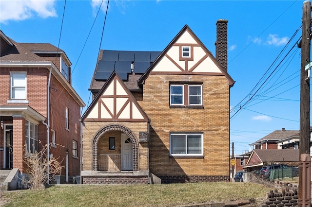 tudor home with a front lawn, brick siding, solar panels, and a chimney