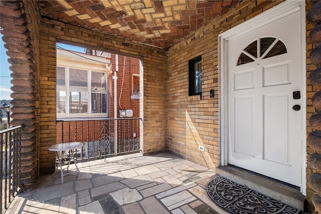 doorway to property with brick siding, log exterior, and a porch