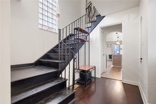 staircase featuring baseboards, arched walkways, and wood-type flooring