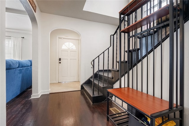 entryway with arched walkways, stairs, baseboards, and wood finished floors