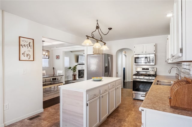 kitchen featuring a kitchen island, arched walkways, a sink, stainless steel appliances, and light countertops