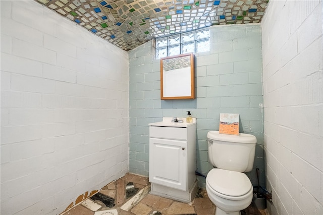 bathroom with vanity, concrete block wall, and toilet