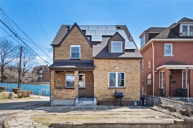 view of front of house featuring brick siding, roof mounted solar panels, and roof with shingles