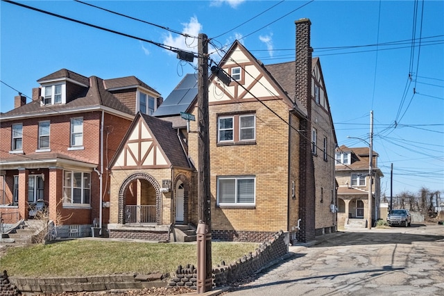 tudor-style house featuring brick siding, roof with shingles, a front yard, a chimney, and driveway