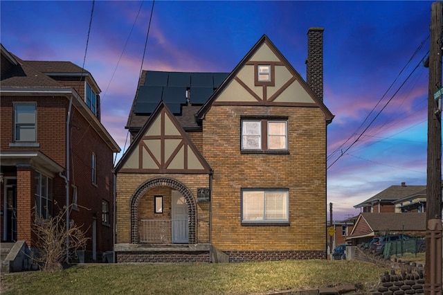 view of front of property with stucco siding, a yard, brick siding, solar panels, and a chimney