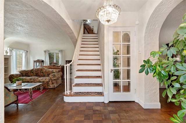 staircase featuring a textured ceiling, arched walkways, an inviting chandelier, baseboards, and a textured wall