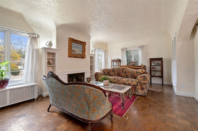 living room with radiator, a fireplace, a wealth of natural light, and a textured ceiling