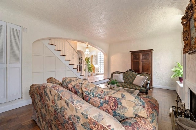 living area featuring a fireplace with raised hearth, stairway, a textured wall, arched walkways, and a textured ceiling