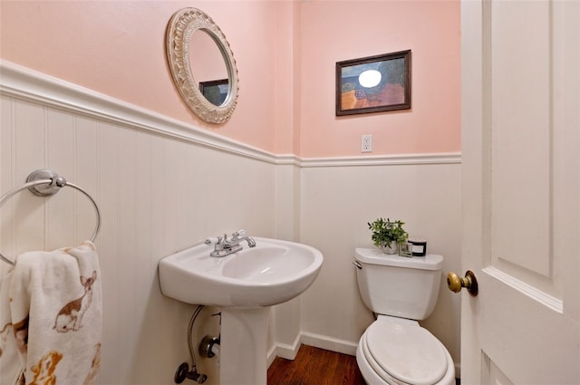 half bath with a wainscoted wall, toilet, and wood finished floors