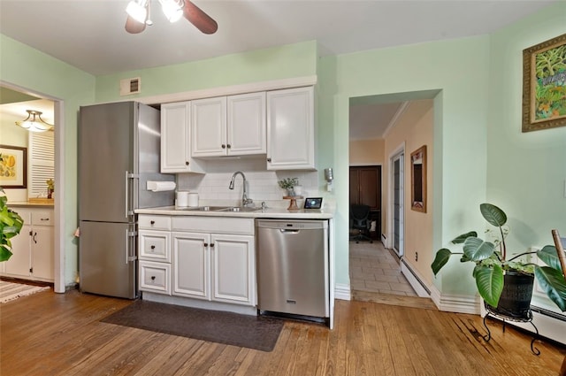 kitchen with light countertops, appliances with stainless steel finishes, wood finished floors, white cabinetry, and a sink