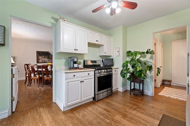 kitchen featuring ceiling fan, light countertops, white cabinets, stainless steel gas range oven, and light wood-type flooring