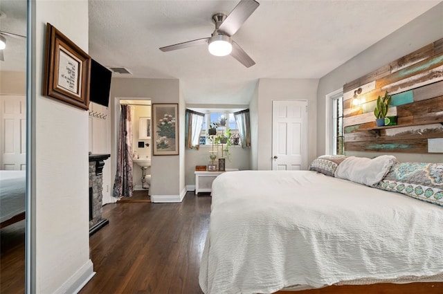 bedroom featuring visible vents, baseboards, dark wood finished floors, a stone fireplace, and a ceiling fan