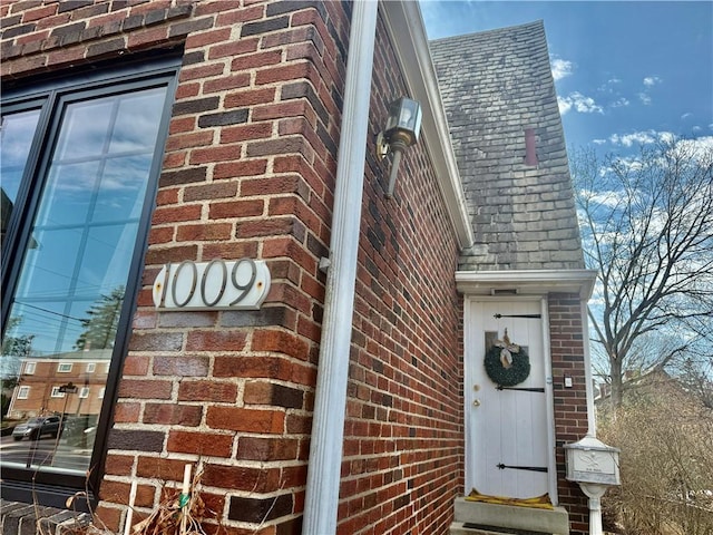 view of exterior entry with brick siding and a shingled roof