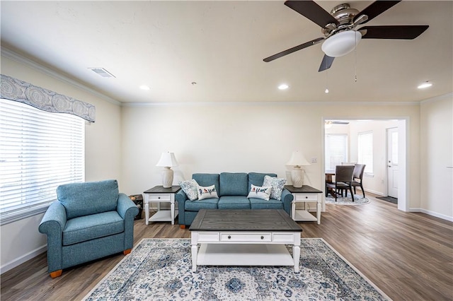 living area with visible vents, wood finished floors, baseboards, and ornamental molding