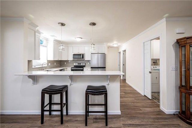 kitchen featuring a peninsula, washer / clothes dryer, a sink, appliances with stainless steel finishes, and white cabinetry