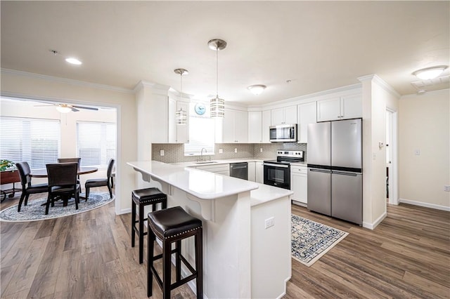 kitchen with a sink, backsplash, appliances with stainless steel finishes, a peninsula, and crown molding