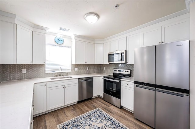 kitchen featuring visible vents, a sink, wood finished floors, stainless steel appliances, and white cabinets