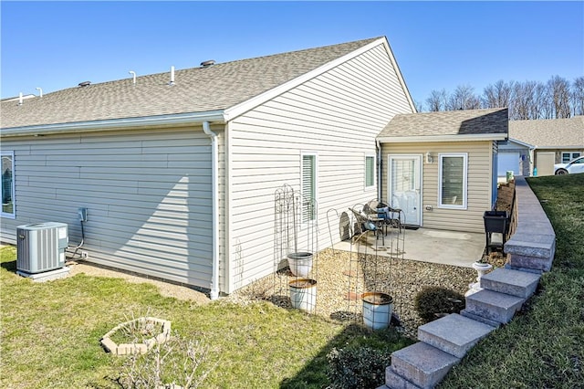 rear view of property with a patio area, central air condition unit, a lawn, and a shingled roof