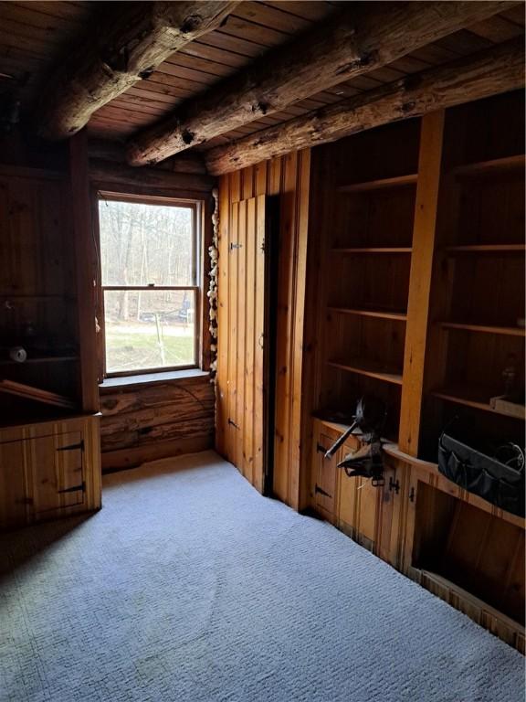 interior space featuring beam ceiling, carpet, wooden ceiling, and wooden walls