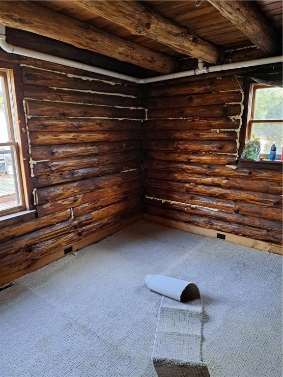 unfurnished room featuring dark colored carpet, log walls, beam ceiling, and wood ceiling