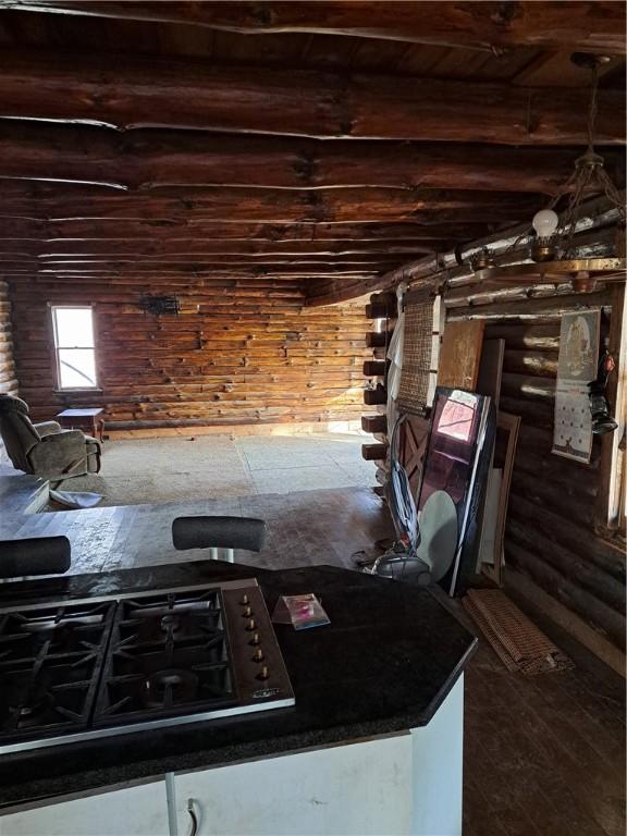 interior space featuring dark countertops, beamed ceiling, black gas stovetop, and log walls