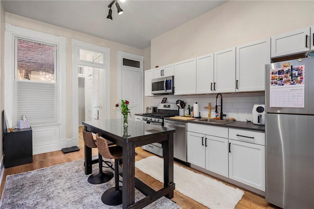 kitchen featuring light wood-style flooring, a sink, appliances with stainless steel finishes, dark countertops, and tasteful backsplash