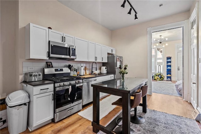 kitchen with light wood-style flooring, a sink, dark countertops, stainless steel appliances, and decorative backsplash