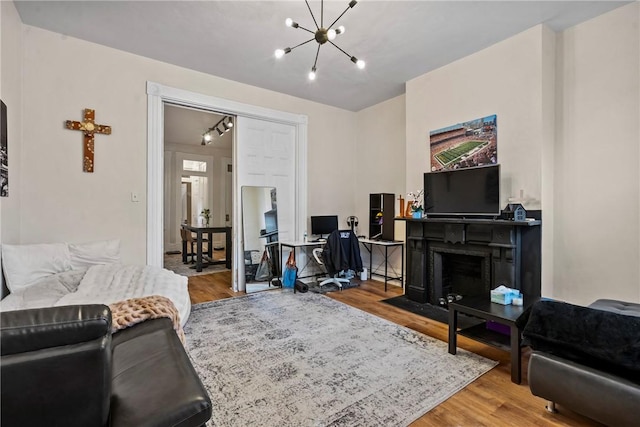 living area featuring a chandelier, a fireplace with flush hearth, wood finished floors, and track lighting