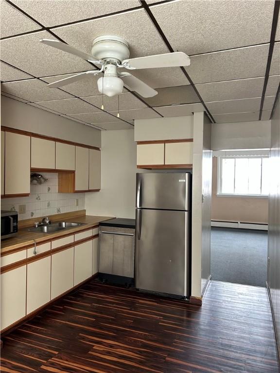 kitchen with dark wood-type flooring, decorative backsplash, a sink, appliances with stainless steel finishes, and a baseboard radiator